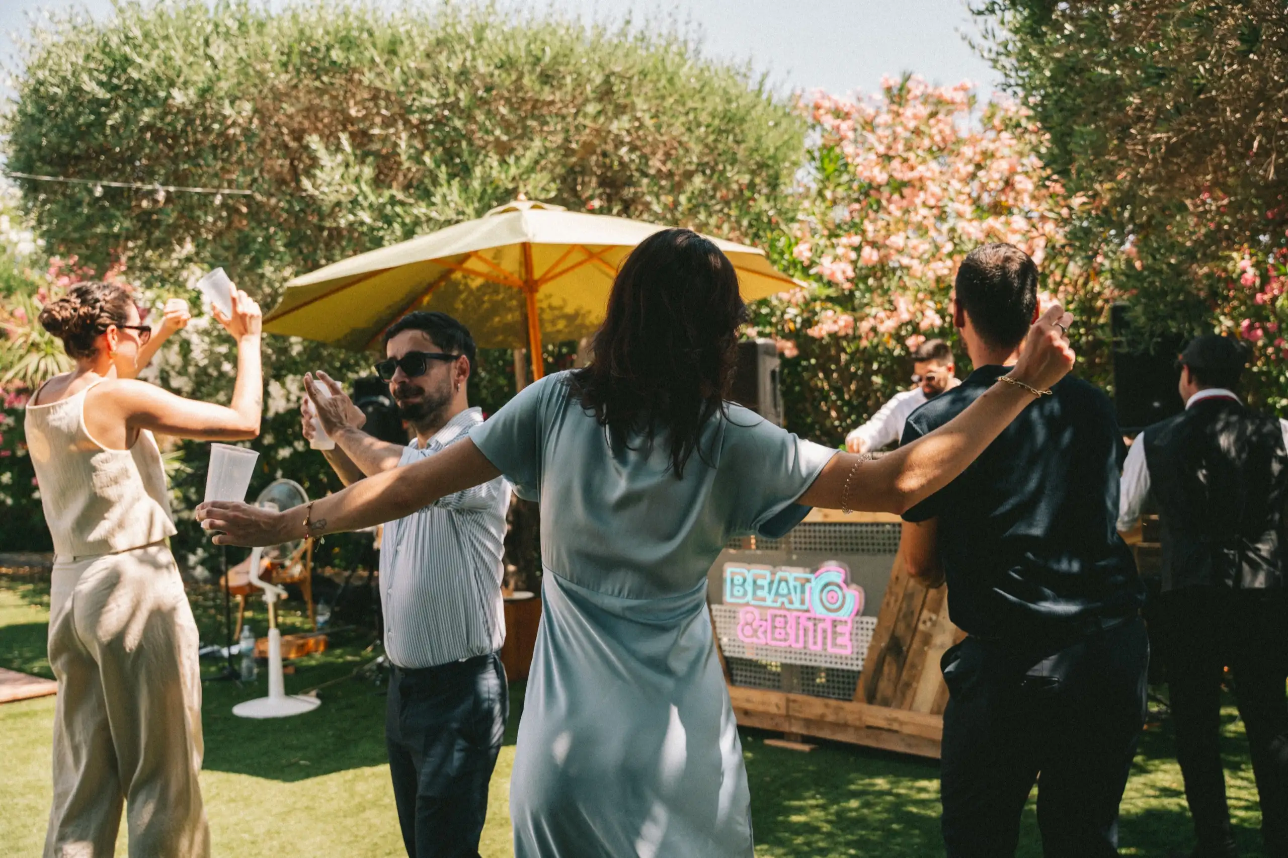 Invitados bailando al sol delante de la cabina del DJ, bajo una sombrilla amarilla