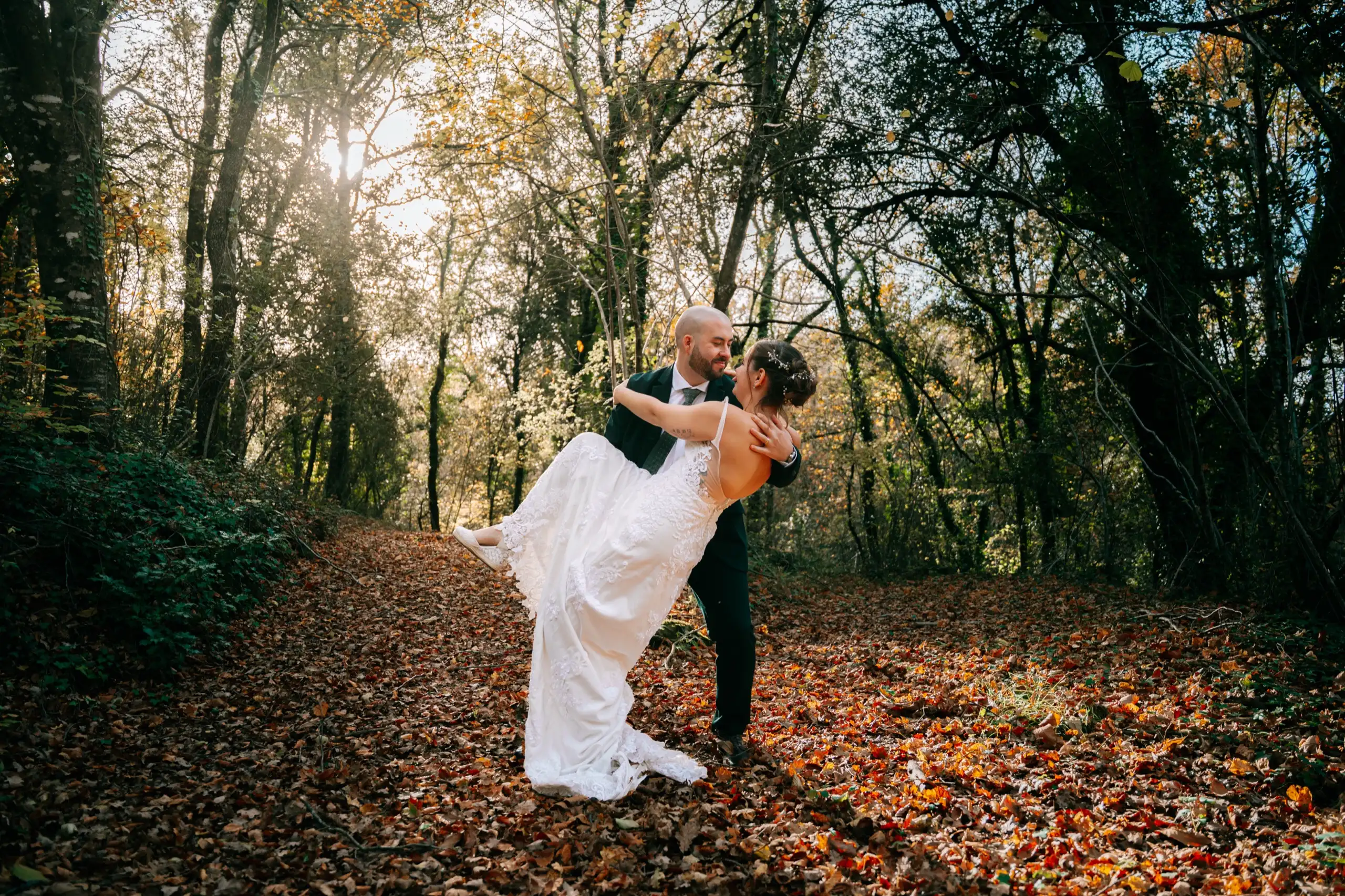 El novio levanta a la novia en un camino del bosque, a contraluz