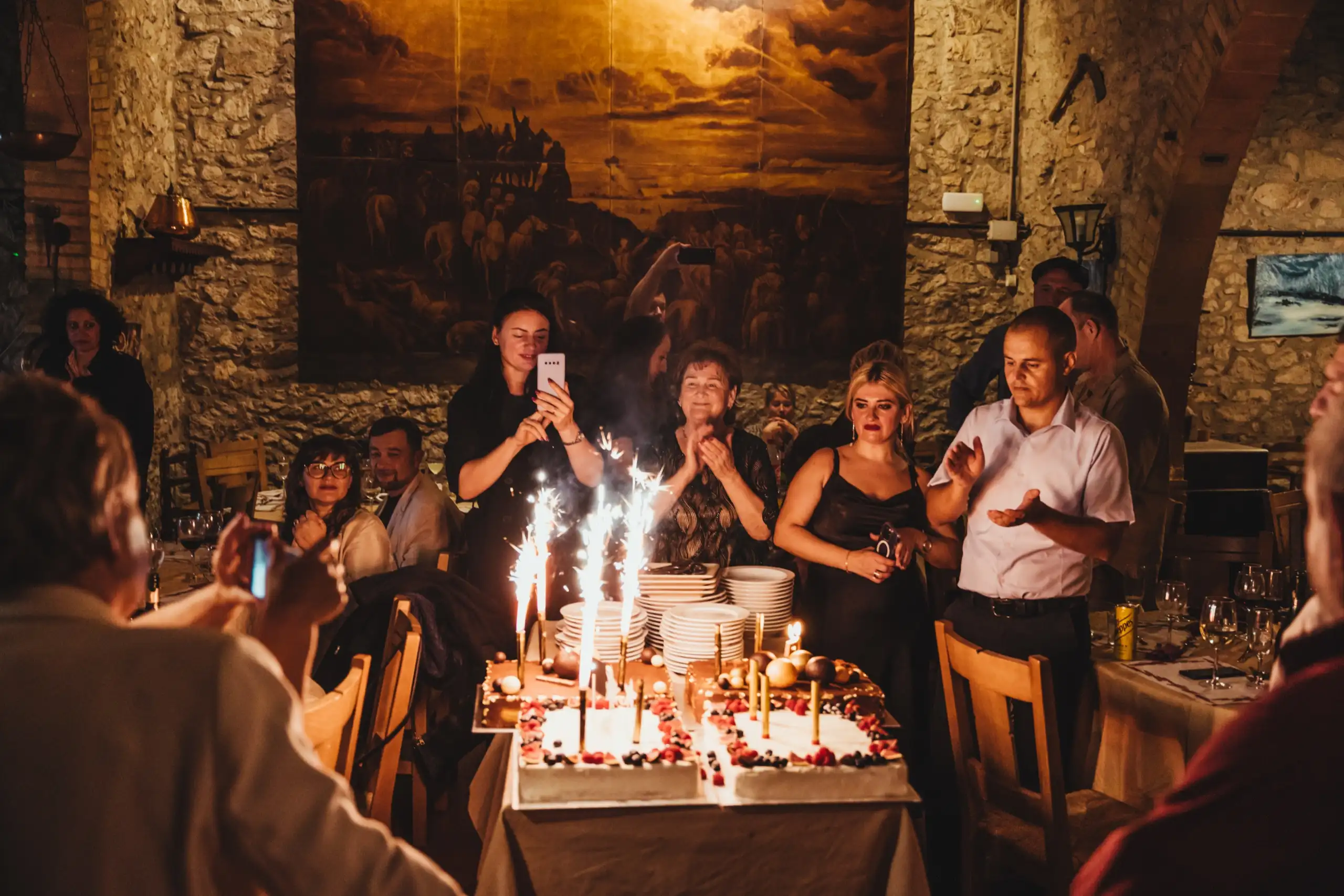 Tarta de cumpleaños con bengalas encendidas y los invitados alrededor